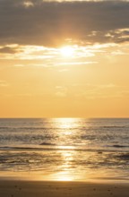 Picturesque sunset over the sea with grey clouds and golden light, sun star, clouds, reflecting