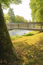 Metal bridge over a river in a sunny park with green trees, Nagold, district of Calw, Black Forest,