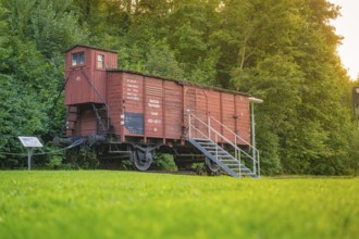 A red goods wagon with steps, green meadow and forest next to it. Nostalgic railway environment,