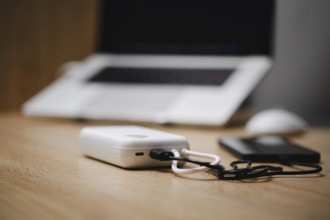 Portable charger connected to a smartphone and laptop setup on a wooden desk during a work session
