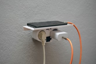 A smartphone rests on a wall-mounted charging station with an electrical outlet below