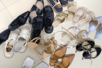 A collection of diverse footwear types is arranged on a light-colored tiled floor. Styles include