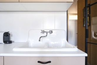 An old-fashioned white sink with a chrome faucet on a countertop in a modern kitchen. The space is