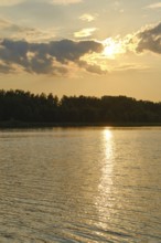 A warm summer afternoon unfolds at the lake, with the sun dipping below the horizon. The water