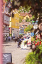 Lively old town street full of people and colourful half-timbered houses, decorated with pennants,