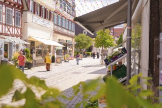 Sunny street in the old town centre with shops and passers-by, surrounded by historic architecture,