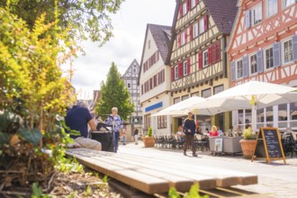 Cosy street scene with half-timbered houses and cafés under parasols on a sunny day, small town