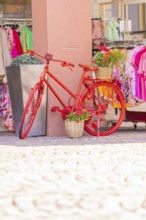 Red bicycle decoratively in front of a clothing shop, surrounded by colourful clothes, small town