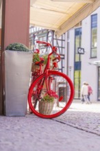 Decorative red bicycle with flower baskets in front of modern buildings in the city centre, small