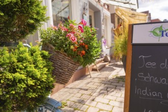 Basket of flowers on a bicycle in front of a shop window in sunny weather, small town of Perle