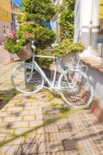 Pale bicycle with lush flower baskets on a sunny street, small town of Perle Calw, district of