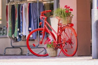 Red bicycle with flowers in a basket in front of a shop window of a clothing shop in the city,