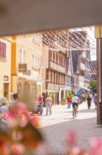 Passers-by and a cyclist in a lively old town street with traditional houses and shops, small town