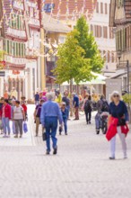 People stroll through a charming, sunny pedestrian zone in an old town with half-timbered houses,