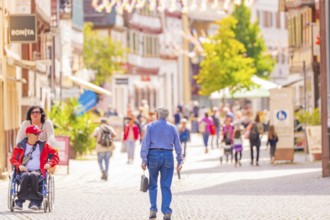 People stroll through a lively, sunny pedestrian zone with historic buildings, small town pearl
