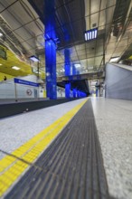 Modern underground station with blue light columns and yellow floor markings, Munich, Germany