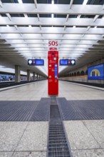 A central SOS pillar in a modern railway station concourse with empty platforms, Munich, Germany