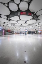 Spacious underground station with modern ceiling and lights, few people scattered around, Munich,