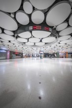 Spacious underground station with modern ceiling and lights, some people scattered in the room,