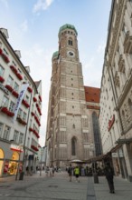 High bell tower of a church surrounded by historical buildings and people on a square, Munich,
