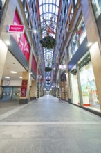 Long shopping arcade with glass roof and illuminated shop windows in an urban atmosphere, Munich,