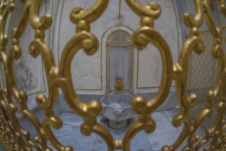Ornate golden gate protecting a marble fountain inside a historical building in istanbul, turkey,