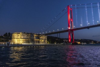 The illuminated suspension bridge over bosphorus strait paints the istanbul night sky red, creating