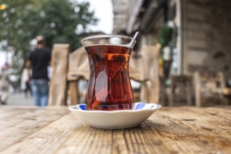 Steaming turkish tea, served in a tulip shaped glass, sits on a wooden table in a cafe in istanbul,