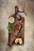 Fried rainbow trout, with herbs and citrus fruits, on a wooden chopping board, top view