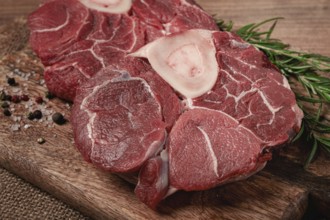 Knuckle on the bone, raw meat for ossobuco, on a wooden chopping board, with a sprig of rosemary,