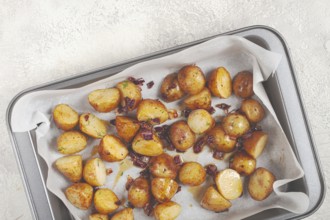 Golden-brown roasted potatoes are arranged on a baking tray lined with parchment paper. They are