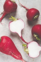 Bright red radishes are arranged on a counter, with one radish cut in half to reveal the crisp