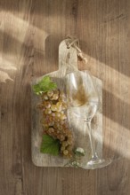 A sprig of white grapes, on a wooden board, with a glass of white wine, top view, natural lighting,