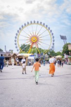 People on a square in an amusement park with a large Ferris wheel in the background, Olympiapark,