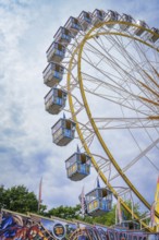 A large section of a Ferris wheel with numerous cabins above a fairground attraction, Olympiapark,