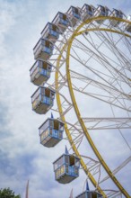 Ferris wheel with blue cabins rises into the cloudy sky, Olympic Park, Munich, Germany