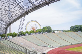 Open stadium with a view of a Ferris wheel in the background and green rows of seats, Olympic Park,