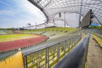 Empty modern stadium with green seats and striking glass roof under a blue sky, Olympiapark,