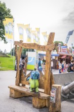 Wooden bench with colourful bear figure and lettering in amusement park with background of