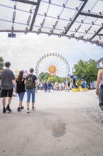 View of a Ferris wheel in an amusement park through a modern construction with many visitors,