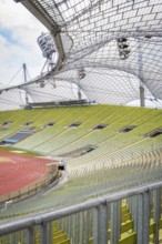 Green stadium with striking metal architecture and empty stands under a clear sky, Olympiapark,