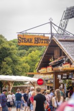 Traditionally designed hut with lettering, surrounded by people and green background, Olympic Park,