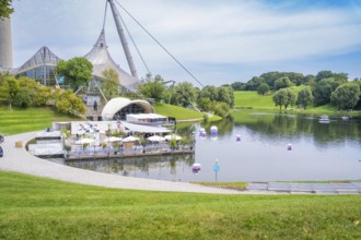 Idyllic landscape with lake, modern pavilion and grassy hills, Olympic Park, Munich, Germany