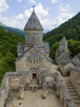 Sacred building with old stone walls, embedded in a wooded landscape under a clear sky, aerial