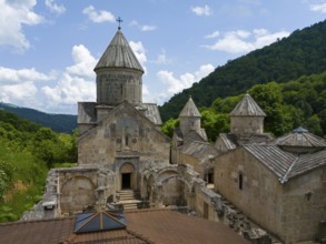 Historic stone monastery surrounded by green forests under a blue sky with clouds, aerial view,