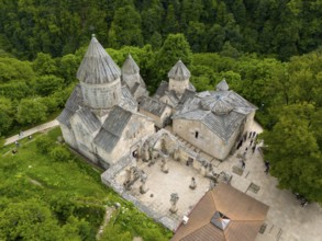 Stone monastery with visitors, surrounded by forest and hilly terrain, aerial view, Haghartsin