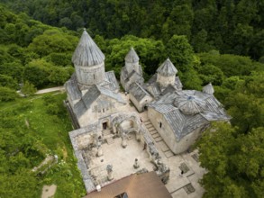 Aerial view of a historic monastery with striking stone architecture, surrounded by forest, aerial
