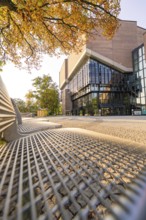 Modern building with glass front, framed by autumnal trees, urban and sunny ambience, Munich,