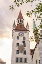 Baroque tower with red roofs and clock in front of a gold-coloured sky, Munich, Germany