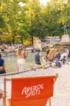 Relaxed atmosphere with people at the fountain and Aperol Spritz, Munich, Germany